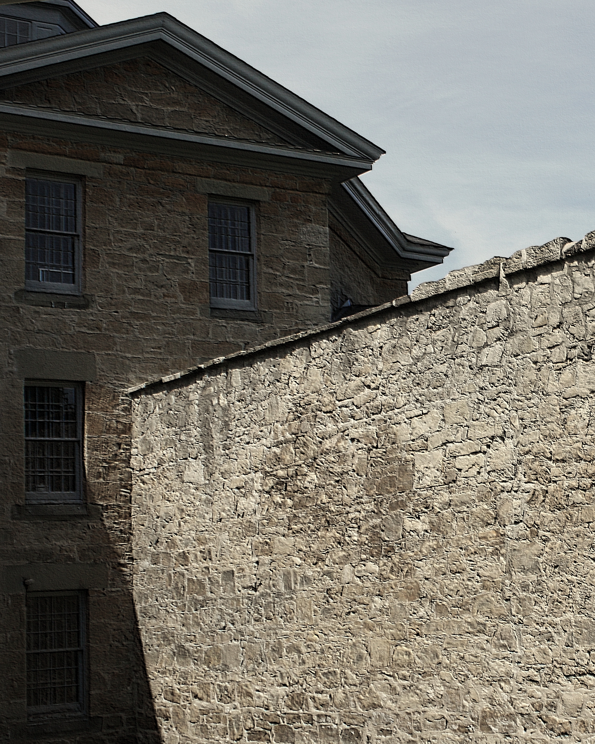 A stone wall, with a gabled building to the left in shadow.