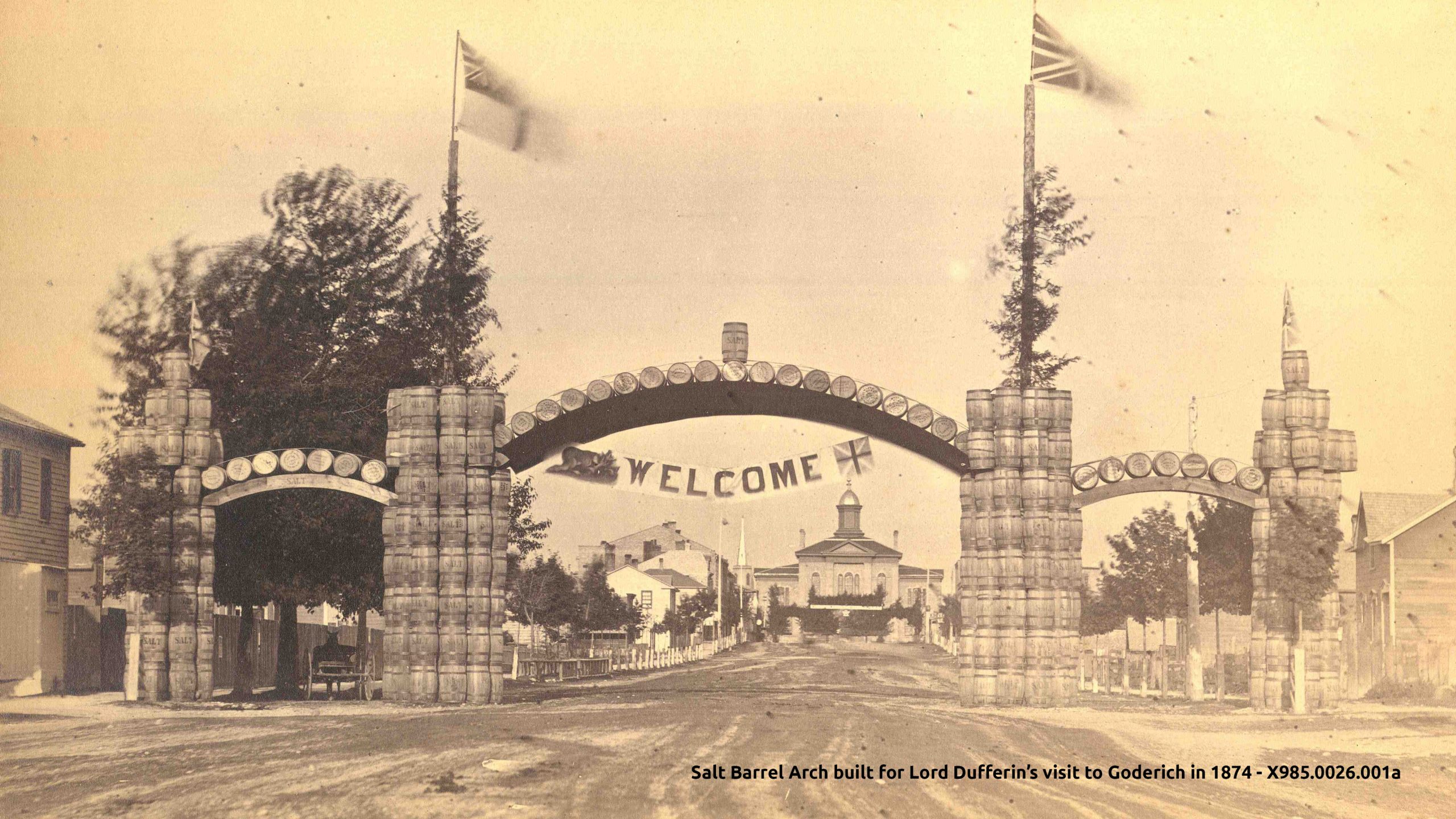 Historic image of salt barrels in an arch welcoming Lord Dufferin to Goderich. The old courthouse is shown in the distance.