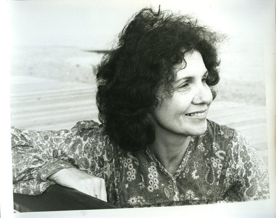 Black & white photo of a smiling Alice Munro, a middle-aged woman with dark curly hair blowing in the wind.