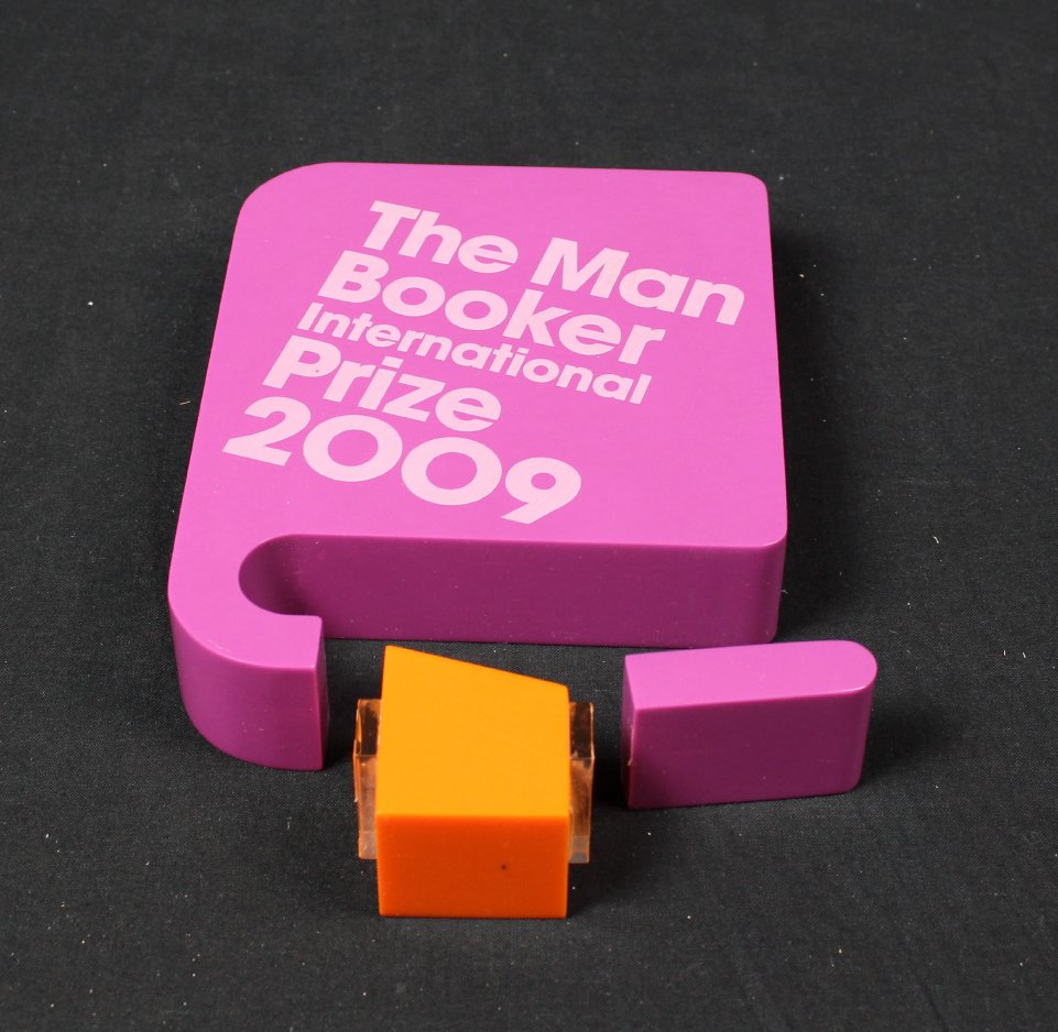 This is a light purple and orange Man Booker International Prize, awarded to author Alice Munro in 2009. It is designed to look like a book with an orange bookmark and is broken into three pieces. 