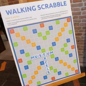 Scrabble board titled "Walking Scrabble." Words on board spell "Museum Excels" 